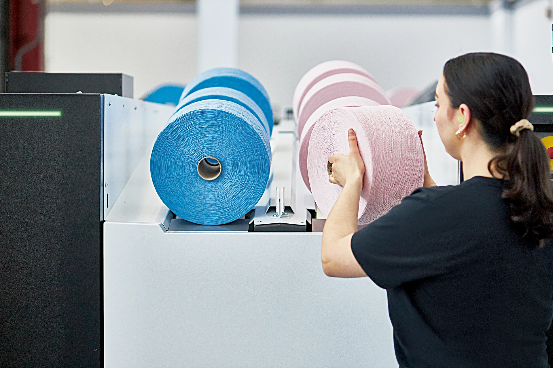 weibliche Person eine rosa Garnspule von einer BD8 Rotorspinn-Maschine nehmend