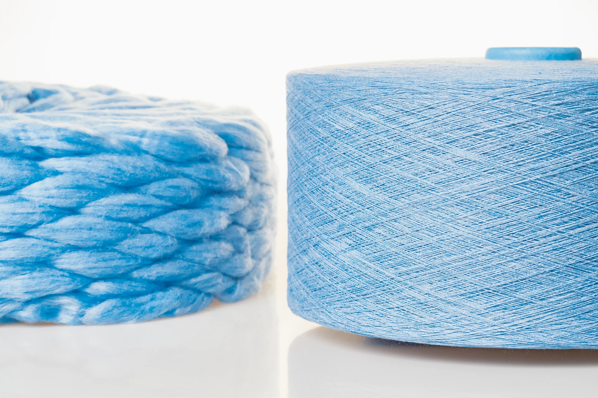 bläuliches Faserband links und das daraus gesponnene Garn auf Spule rechts